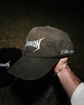 Dark green camp golf cap logo held by a hand against a dark background