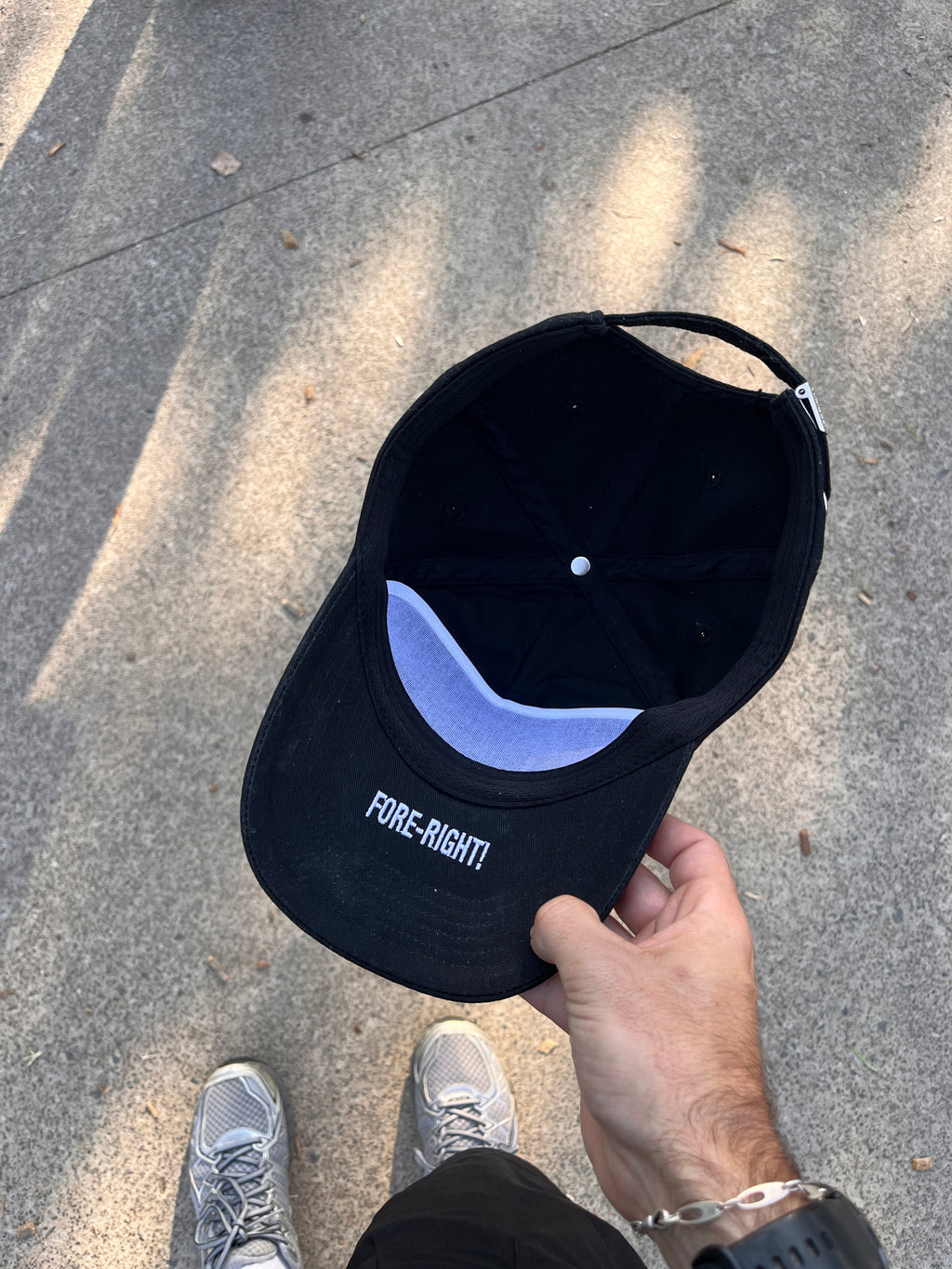 Black golf cap held by a hand on a concrete surface