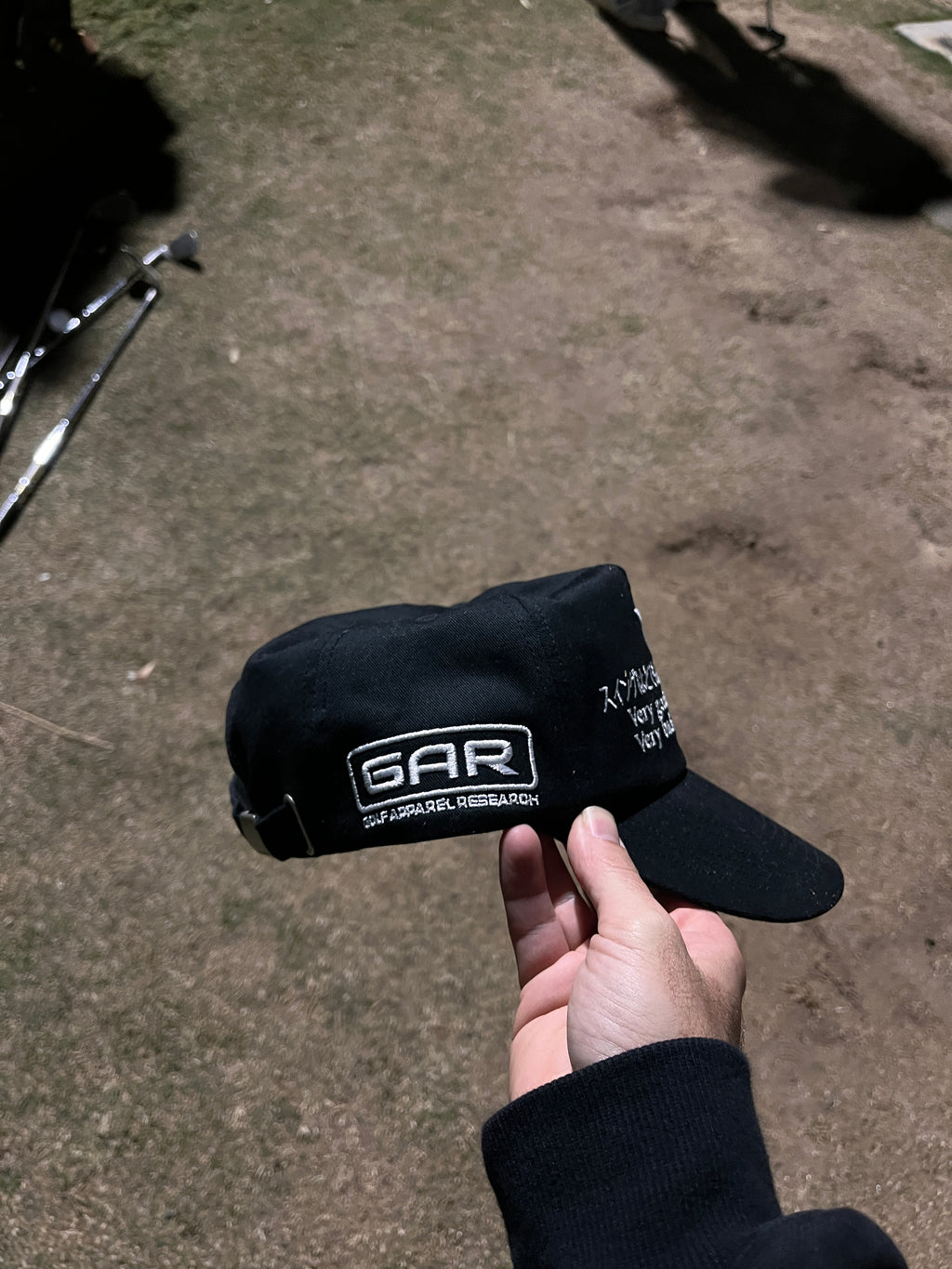 Person holding black golf cap on grassy golf course.