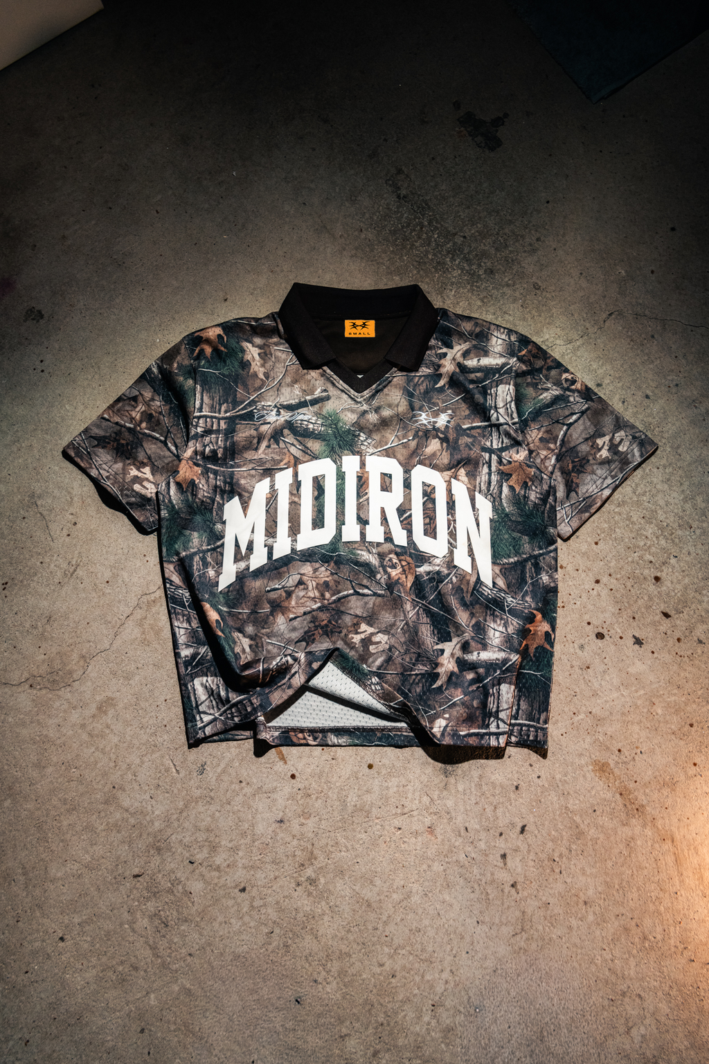 Camouflage polo with 'MIDIRON' branding on a concrete floor