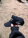 Black golf cap held by a hand on a grassy golf course.